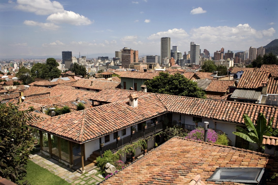 Aerial view of La Candelaria's colonial white-walled houses with terracotta roofs and Bogotá's modern skyline in the background.