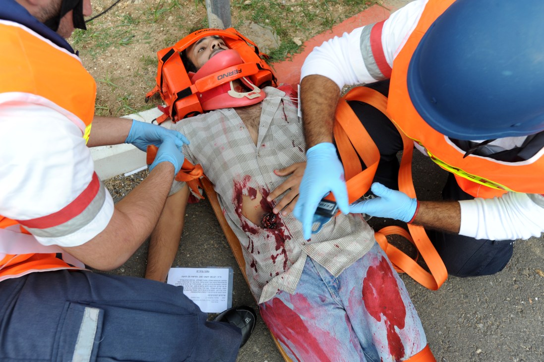 Emergency responders in orange vests and blue gloves treat a simulated casualty lying on the ground during a mass casualty training drill.