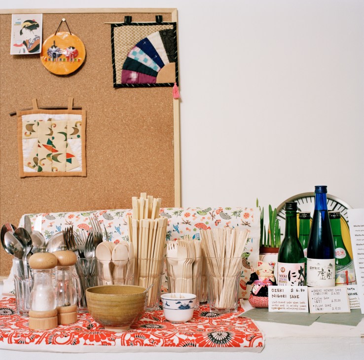 Cha No Ma café counter display with wooden utensils, sake bottles, and decorative items on a floral cloth.