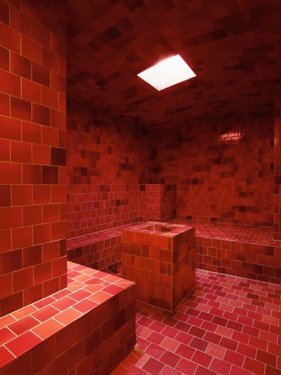 Red tiled steam room with monochromatic mosaic design and skylight at Samedan spa.