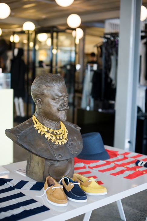Bronze bust sculpture wearing gold necklace displayed with colorful boat shoes in retail store