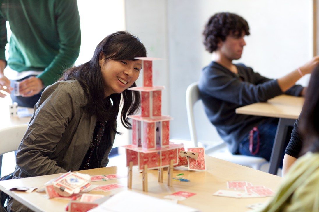Student smiling while building a card tower structure in a design class at Stanford's d.school.