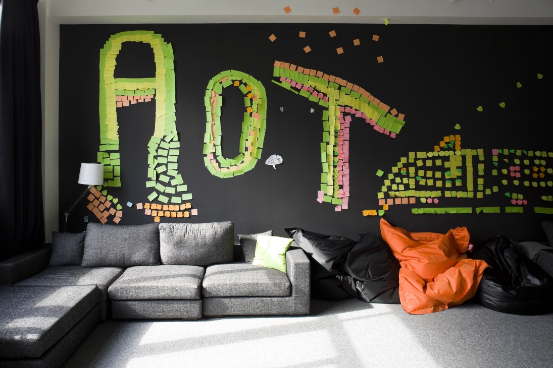 Interior lounge area with grey sofa, orange bean bags, and colorful pixelated wall art.