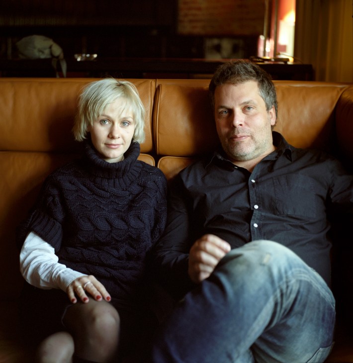 Strelka president Ilya Oskolkov-Tsentsiper sits on a tan leather sofa next to a woman with blonde hair.