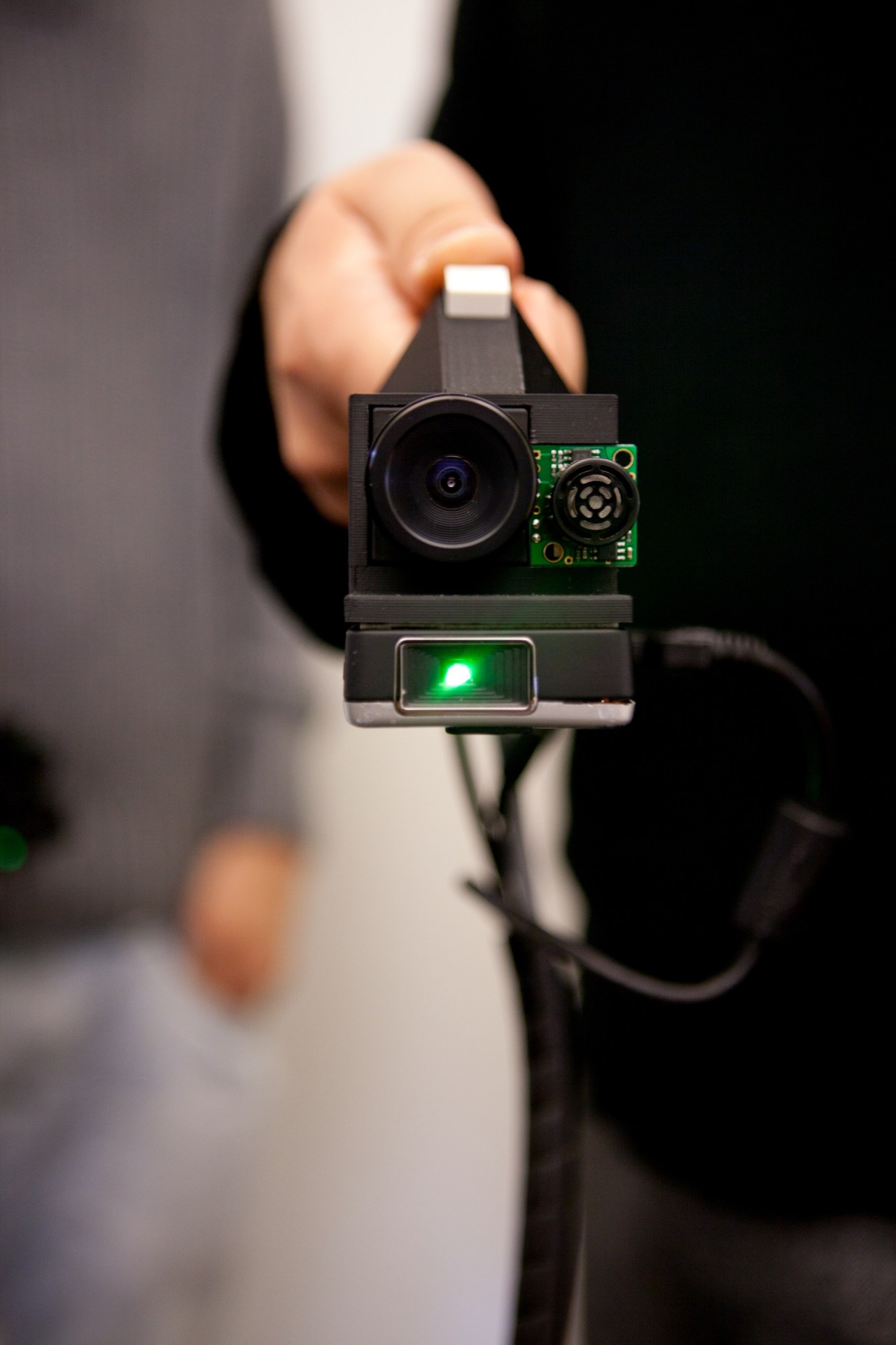 'Side by side' prototype camera device with lens and green circuit board held in hand