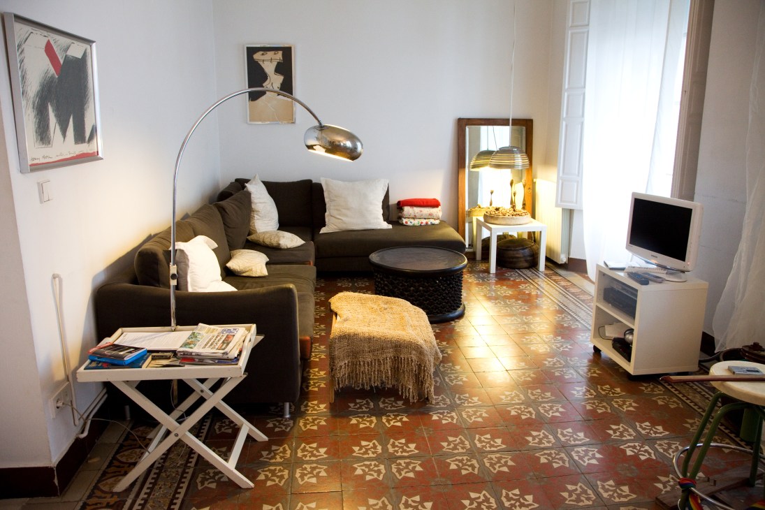 Modern living room with dark sofa, arc lamp, decorative artwork and ornate terracotta floor tiles.