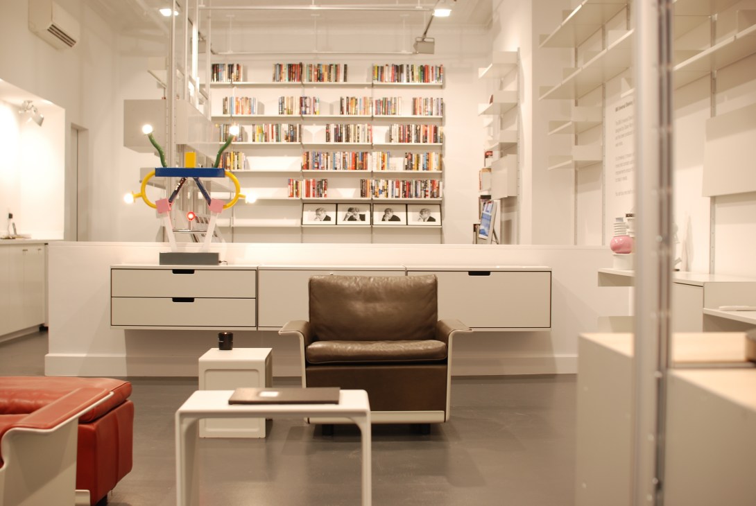 Interior of Vitsoe's New York shop on Bond Street showing white modular shelving systems with books and a brown leather armchair.