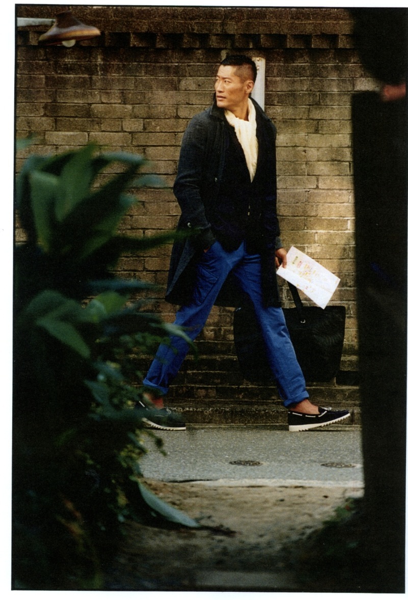 Model wearing a Sacai coat and Comme des Garçons Homme Deux jacket standing against a brick wall.