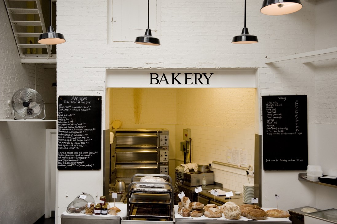 St John bakery section with yellow-painted interior, display counter of fresh bread loaves, and chalkboard menus on white brick walls.