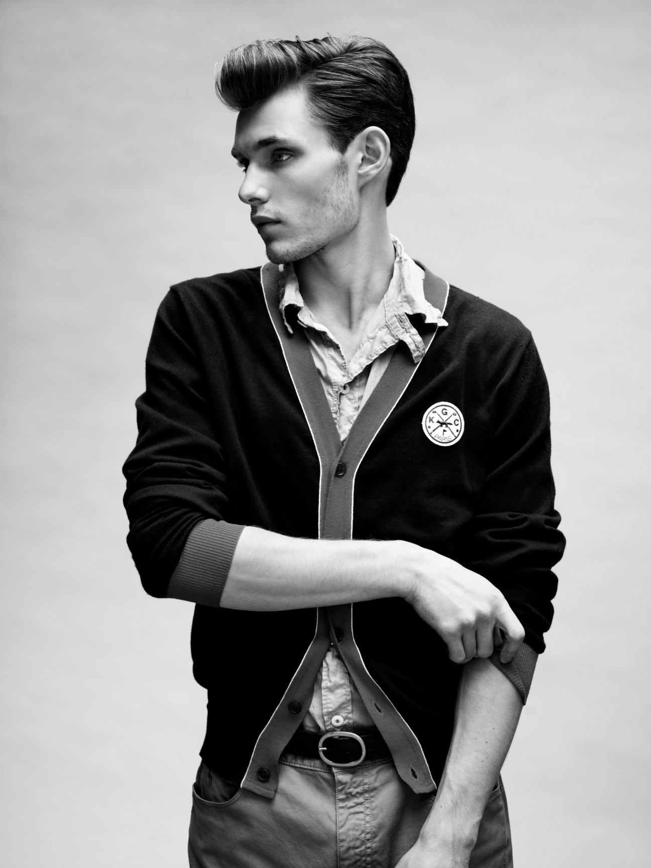 Male model wearing a black cardigan by Kitsuné over a white shirt, styled with belt and trousers.