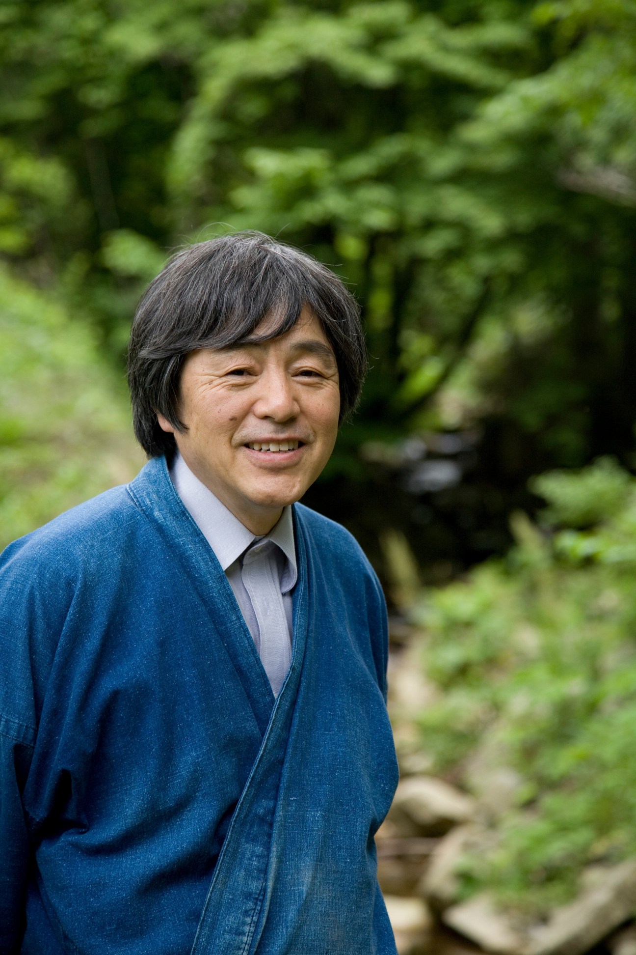 Tadashi Inamoto, a Japanese environmentalist and Oak Village founder, smiles outdoors wearing a blue denim jacket.