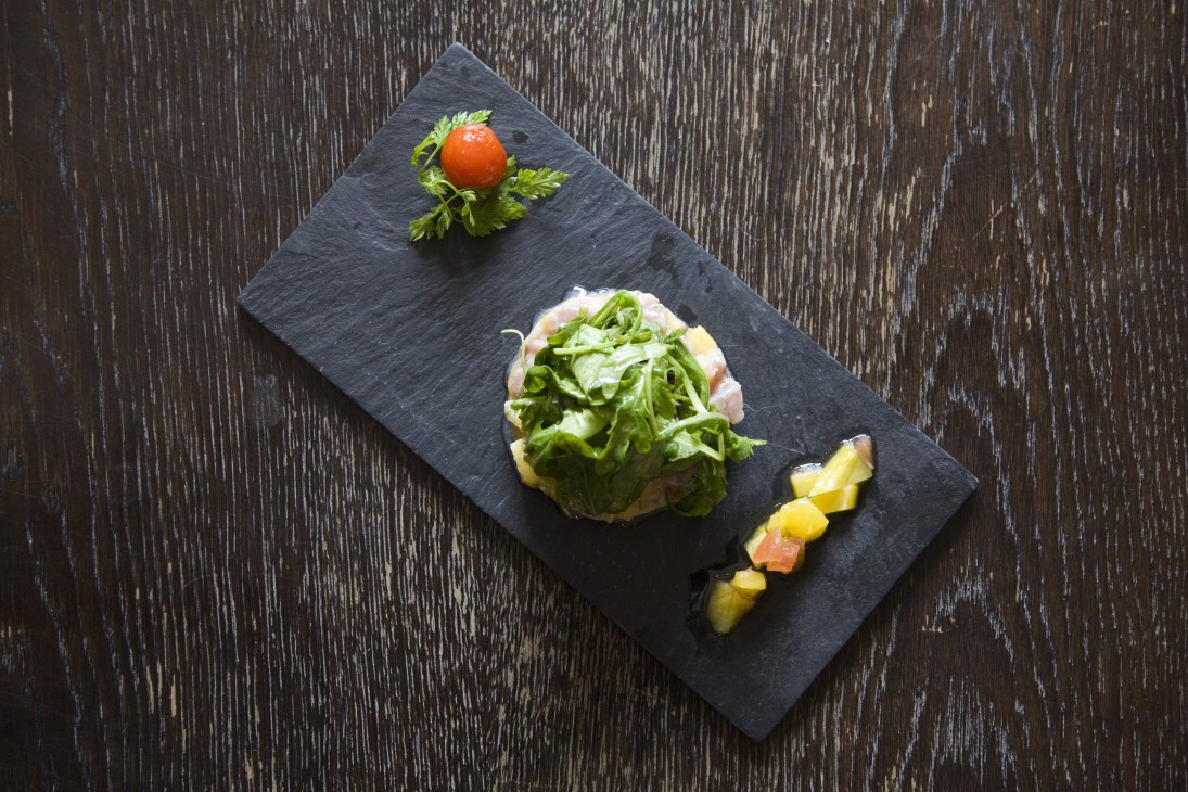 Tartare of tuna with coriander and mango served on a black slate plate with microgreens and diced mango.