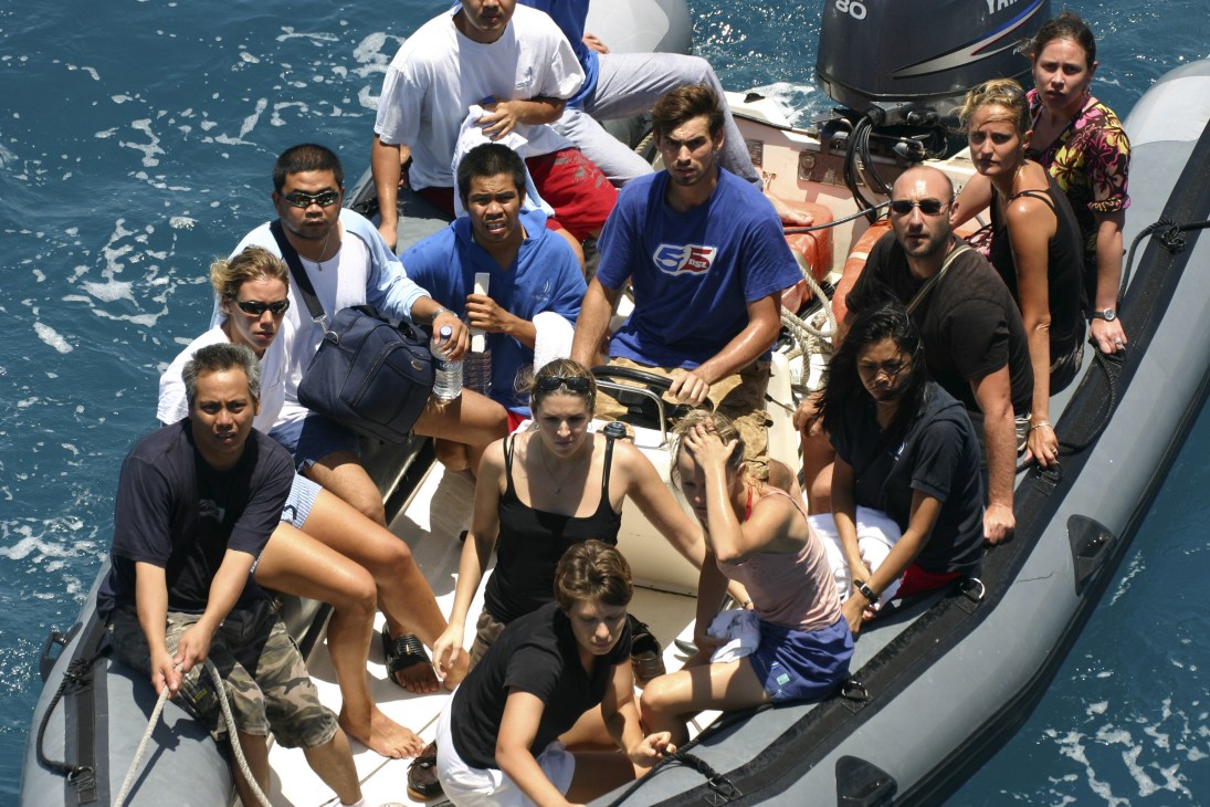 A group of tourists and crew members crowded on a rescue boat in open ocean water.