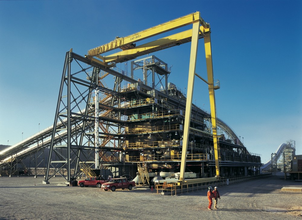 Large yellow industrial crane towers over a multi-level mining facility with steel framework in northern Chile.