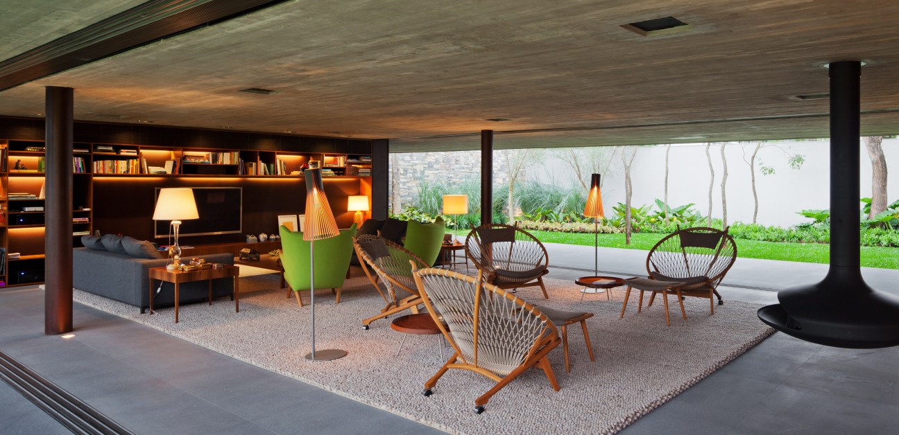Modern open-plan living room with Hans Wegner chairs, built-in shelving, and floor-to-ceiling windows overlooking a garden.