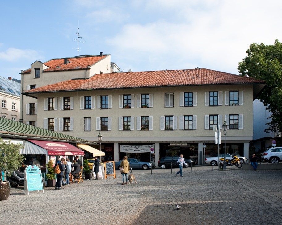 The Viktualienmarkt apartment building in Munich with cream-colored facade, orange roof tiles, and ground-level shops, completed in 1977.