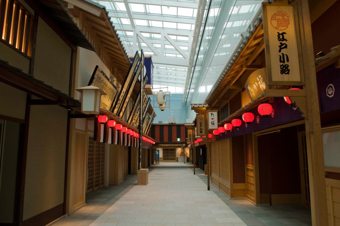 Traditional Japanese wooden storefronts with red lanterns lining a narrow alley in Edo Koji at Haneda Airport.