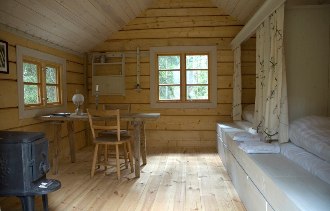 Interior of a timber cabin at Urnatur eco-lodge in Sweden, with wooden walls, windows overlooking forest, and minimal furnishings.