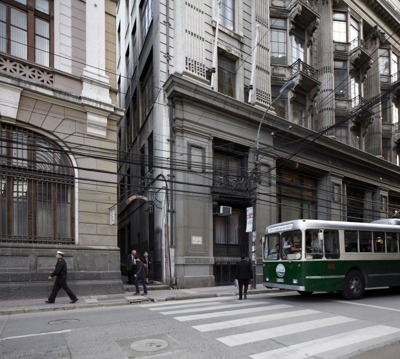 Green and white trolleybus number 802 travels up Calle Prat in Valparaiso, passing Victorian-era buildings with pedestrians on the street.