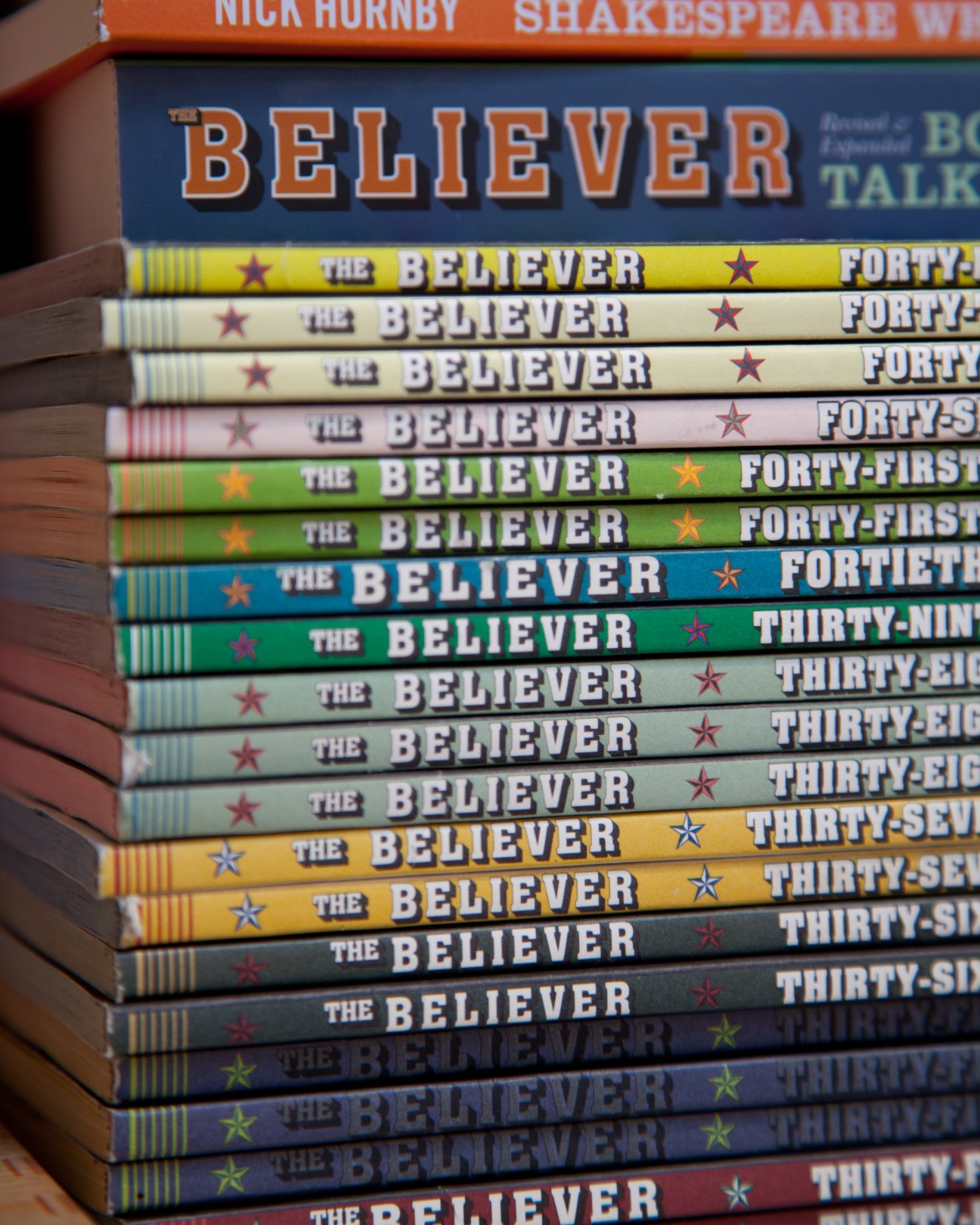 A stack of The Believer magazine issues with colorful spines showing issue numbers and star designs.