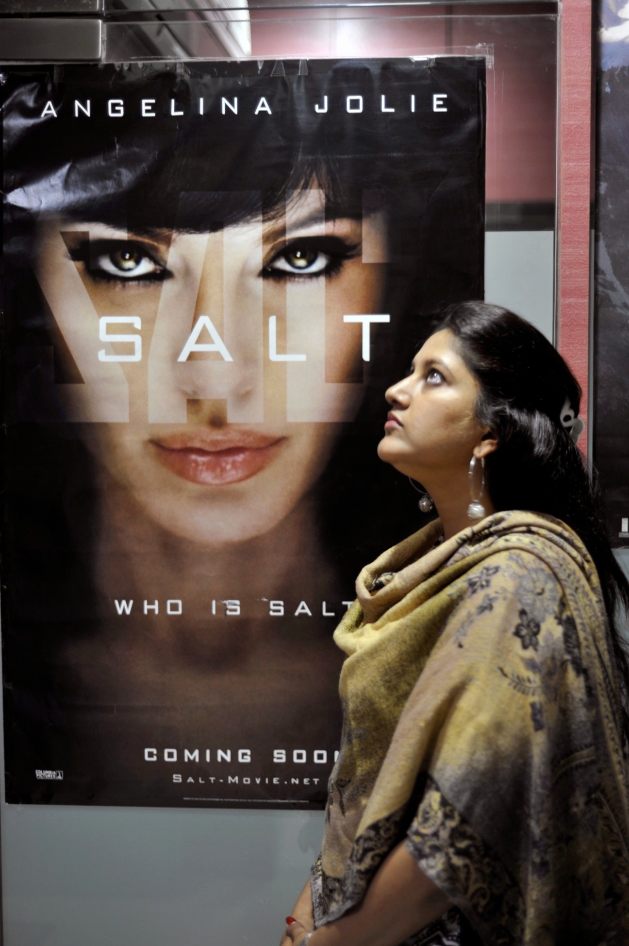 Mona Shetty stands in profile next to a movie poster for 'Salt' featuring Angelina Jolie.