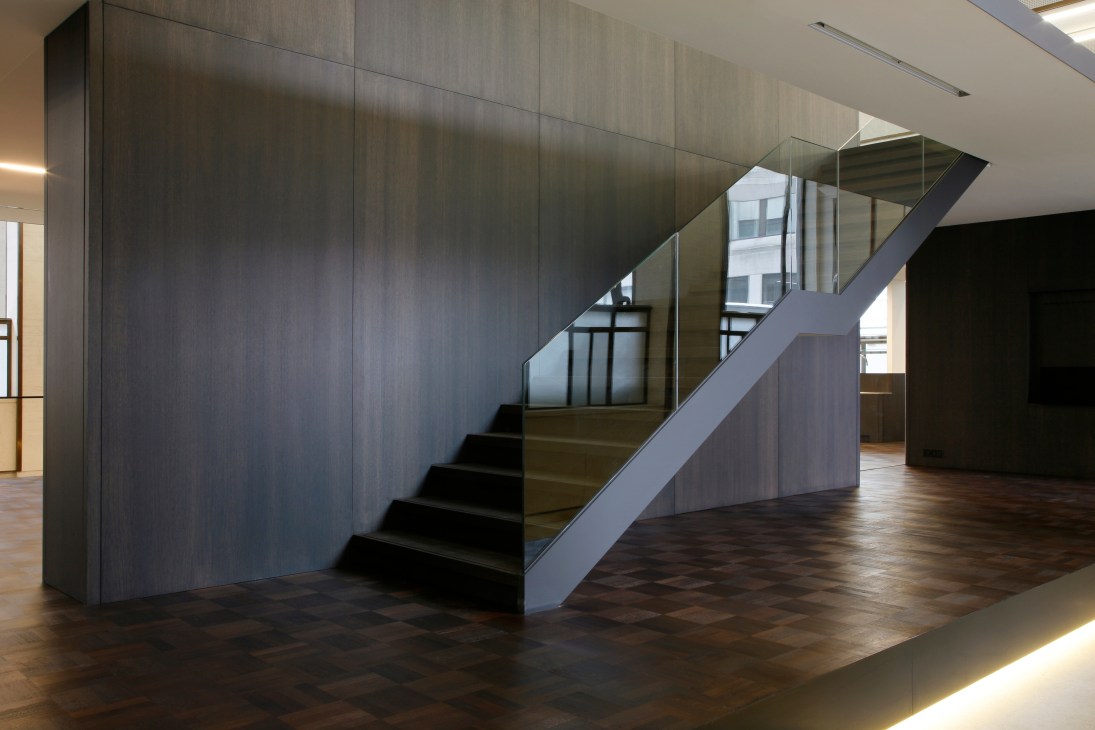 Modern interior staircase with glass railings and wooden steps in the Flemish Parliament's redesigned De Loketten counter room.