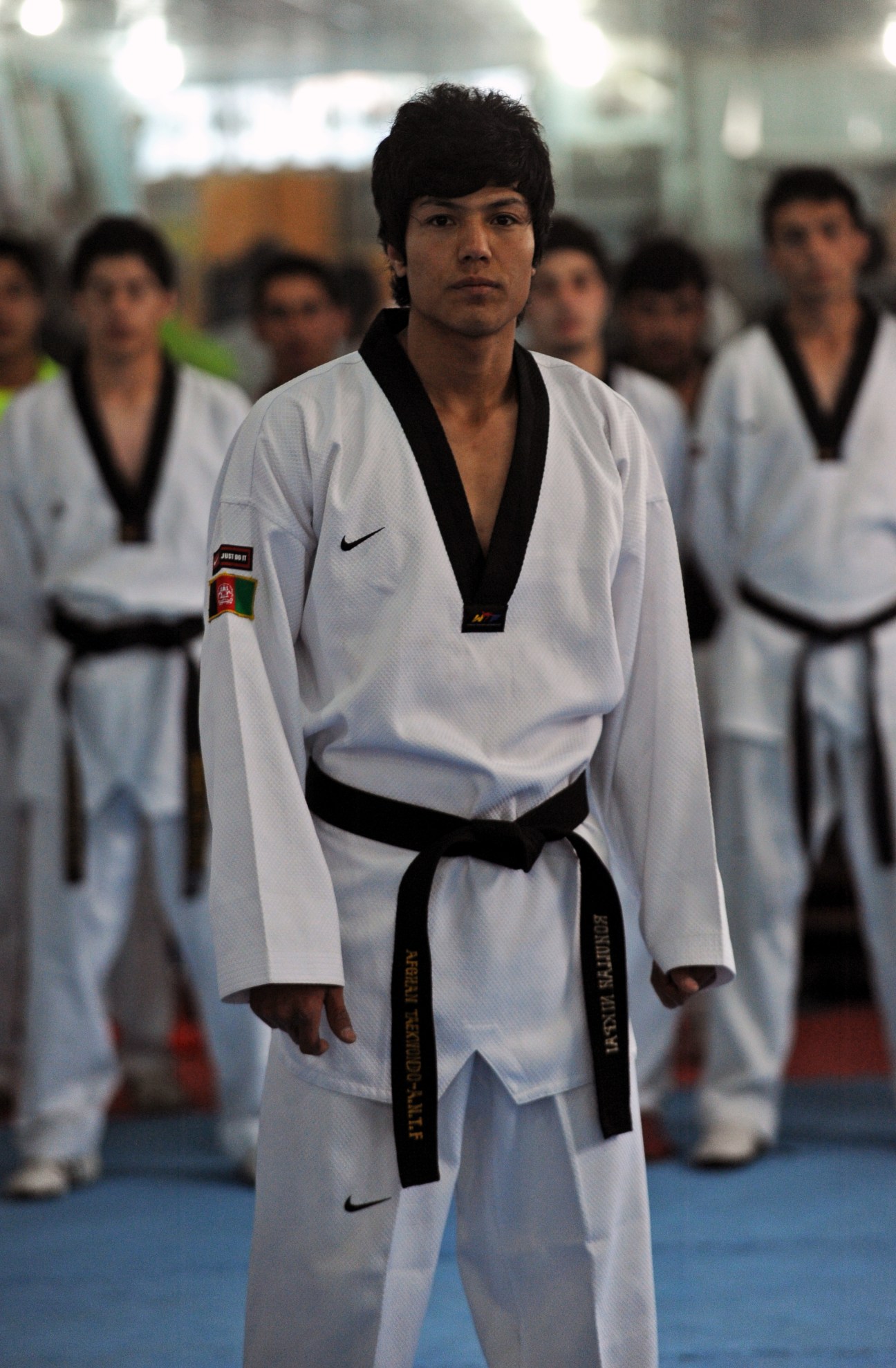 Rohullah Nikpai stands in taekwondo uniform with other athletes blurred in the background.