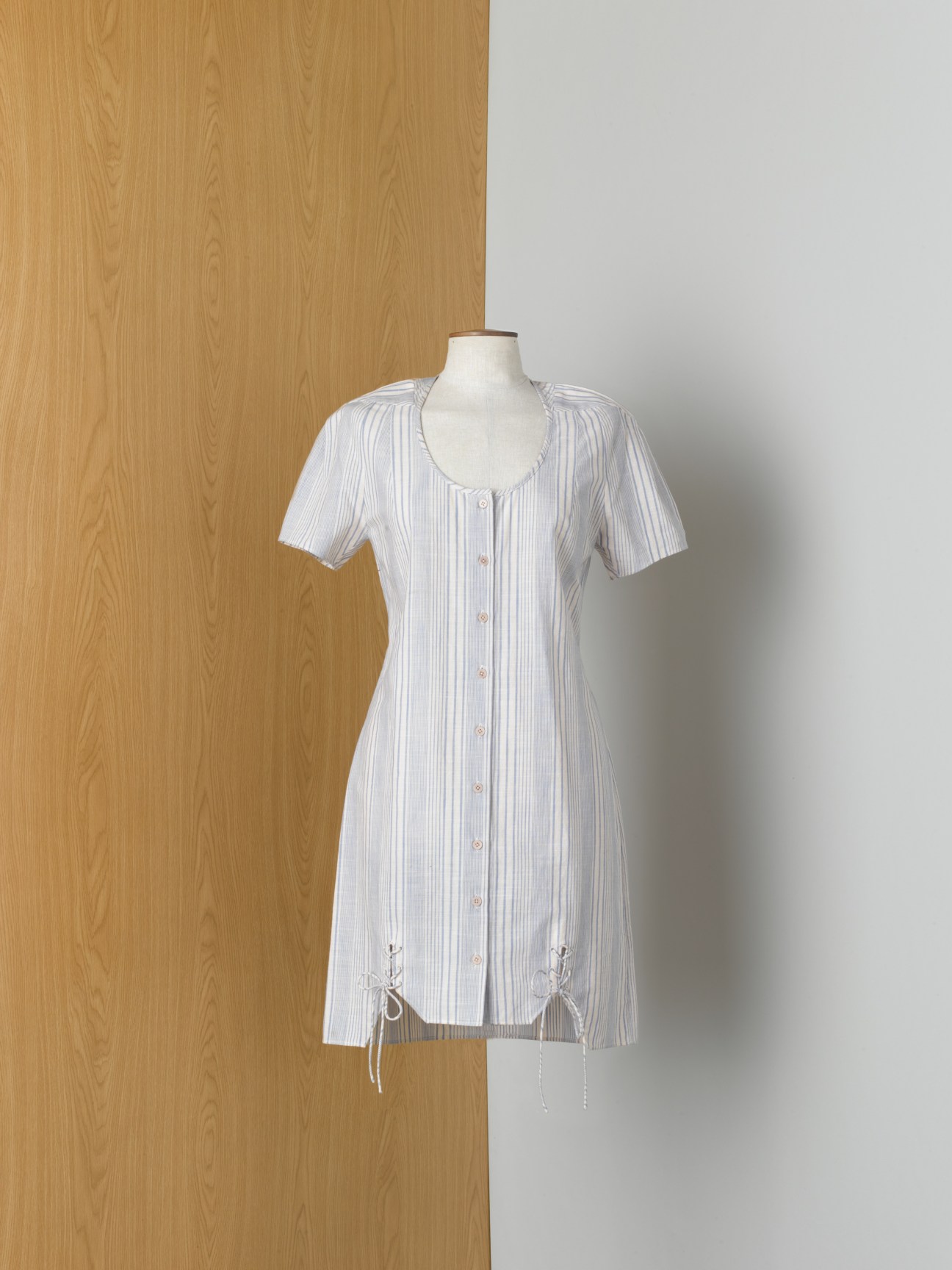 White pinstriped short-sleeve button-front dress on mannequin against wooden backdrop.