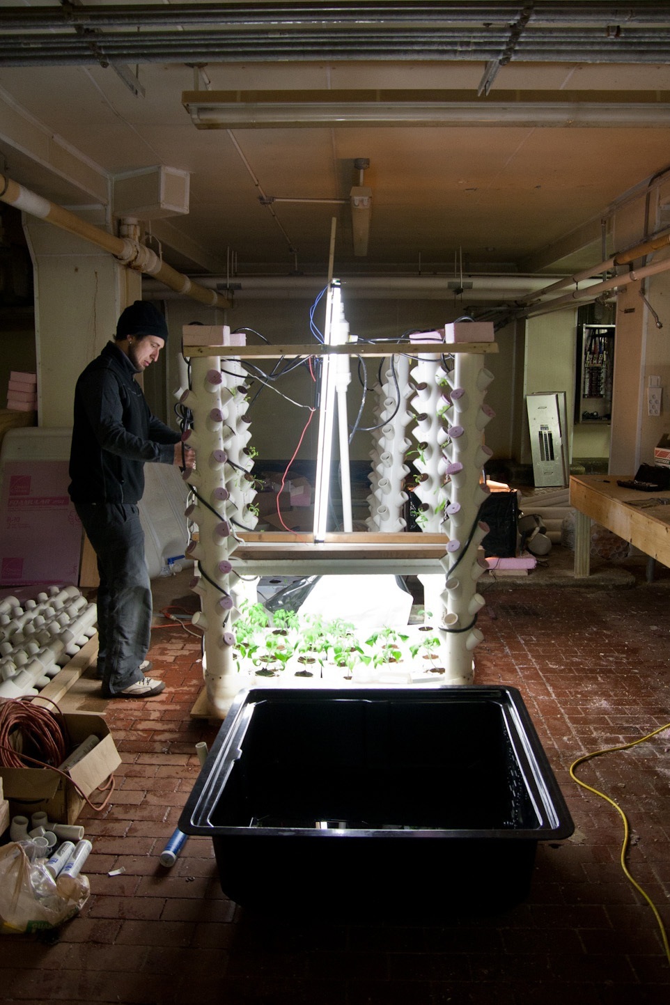 Person inspecting vertical hydroponic growing system with LED lights in industrial warehouse space.