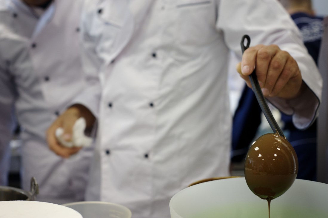 Chef holding a spoon dripping brown gelato mixture over a bowl during gelato preparation.
