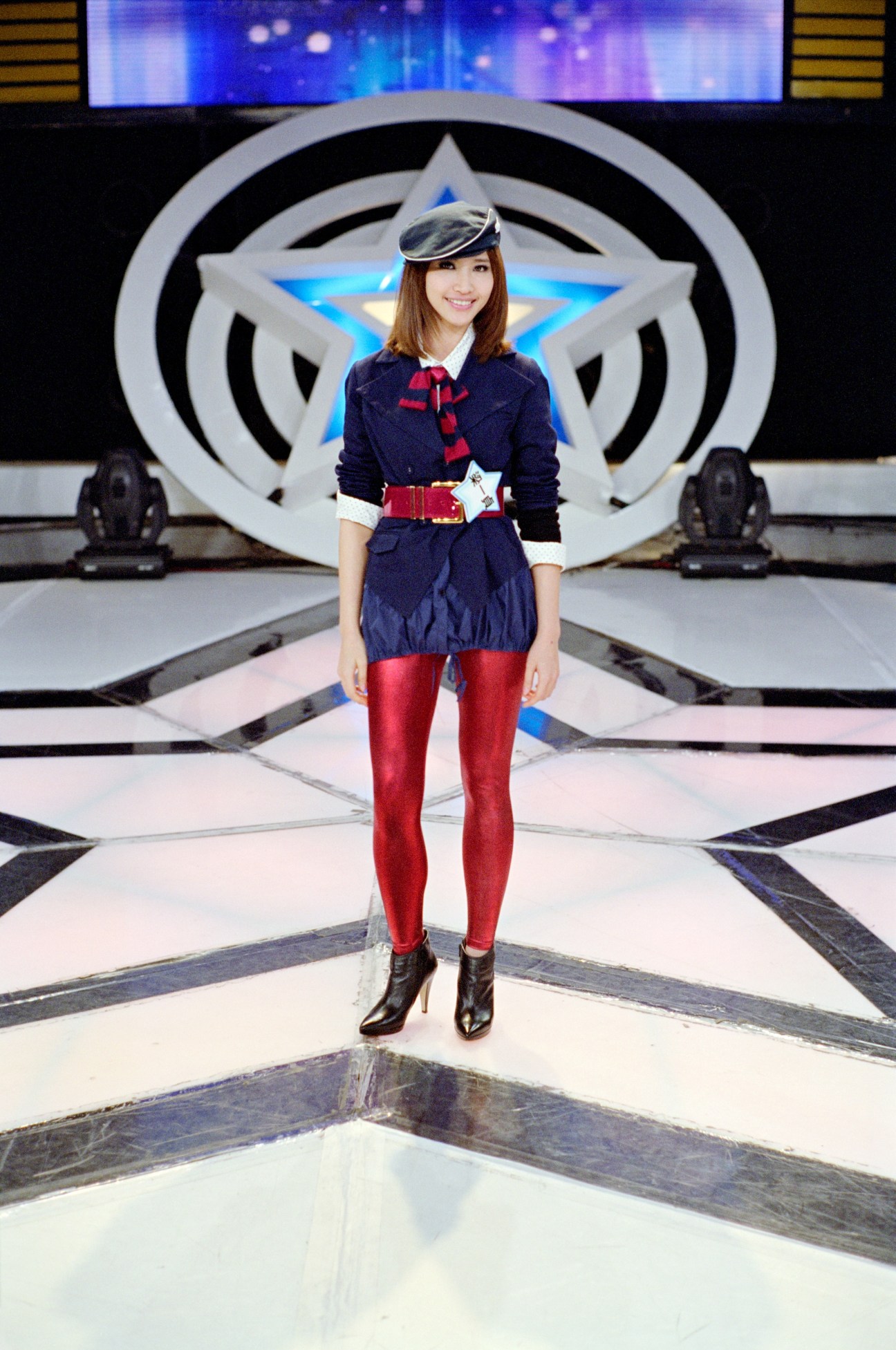 Young woman in navy and red outfit standing on 'One Million Star' TV set stage with star-shaped backdrop.