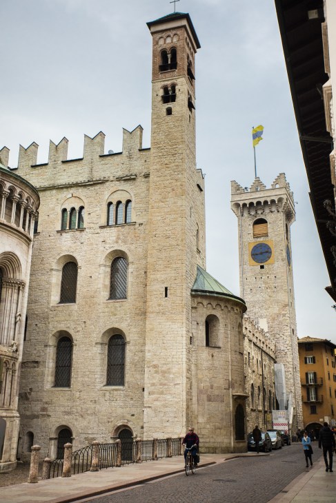 Medieval stone cathedral with crenellated tower in Trento's main piazza, featuring gothic architecture.