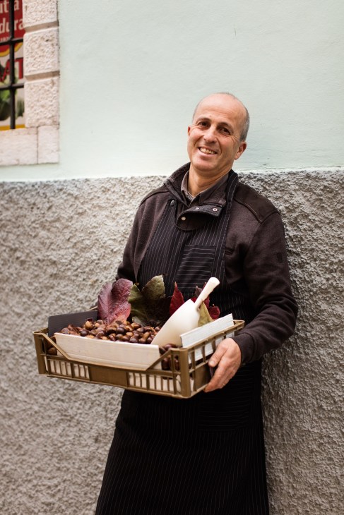 Stefano Demattè, owner of the Demattè fruit and vegetable shop, holds a crate of produce including nuts and vegetables.