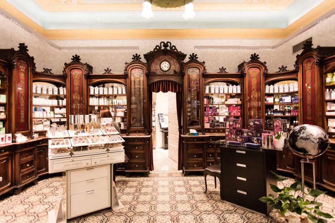 Interior of Gallo Pharmacy with ornate wooden cabinetry, decorative inlays, and shelves displaying beauty and pharmaceutical products.