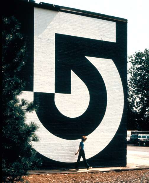 Large-scale Channel 5 logo painted on brick wall with person standing in front for scale