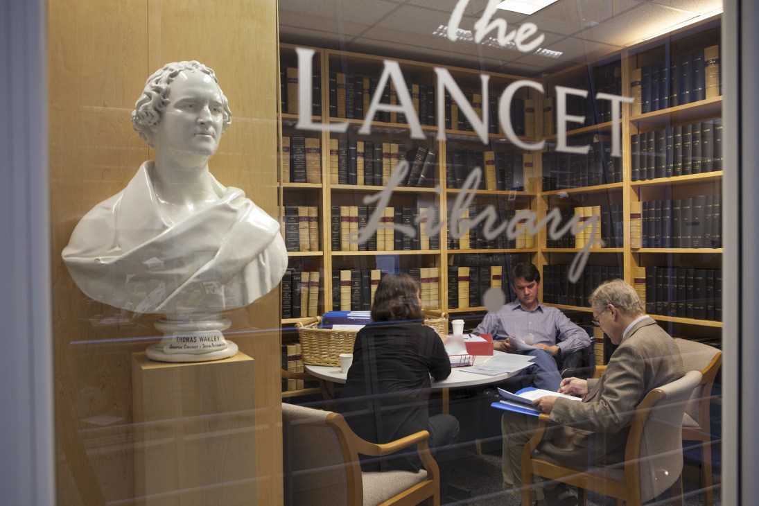 The Lancet library with shelves of bound journals, a bust of founder Thomas Wakley, and staff working at a table.