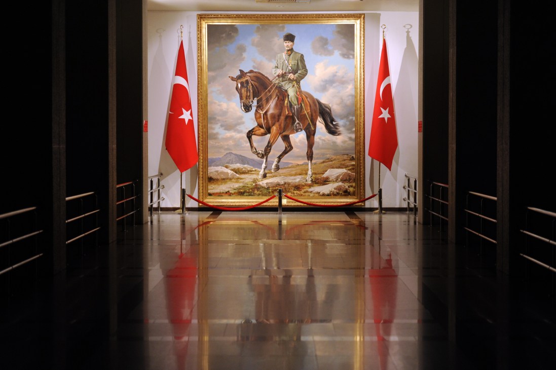 Portrait of Atatürk on horseback in a gold frame, flanked by Turkish flags in a formal hallway.
