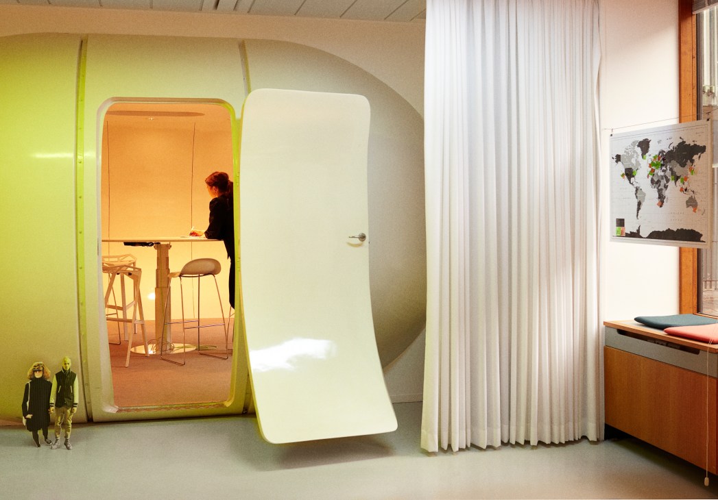 A woman works at a standing desk inside The Mind, a bright lime-green pod-shaped meeting space with orange interior at Mindlab.