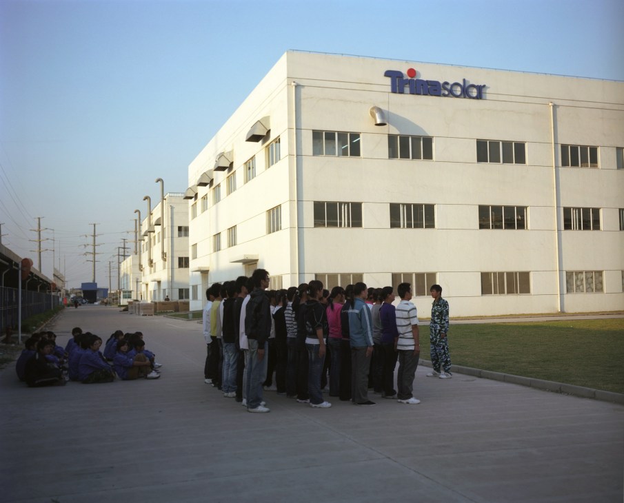 New employees gather in front of Trina Solar's modern white factory building in Changzhou.