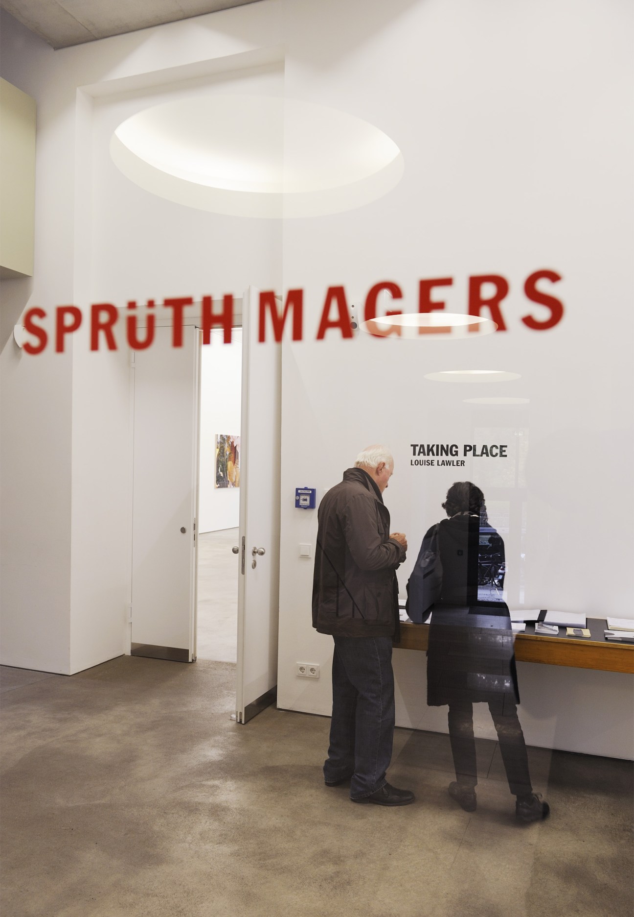 Interior of Sprüth Magers Berlin gallery with red signage and visitors viewing Louise Lawler exhibition.