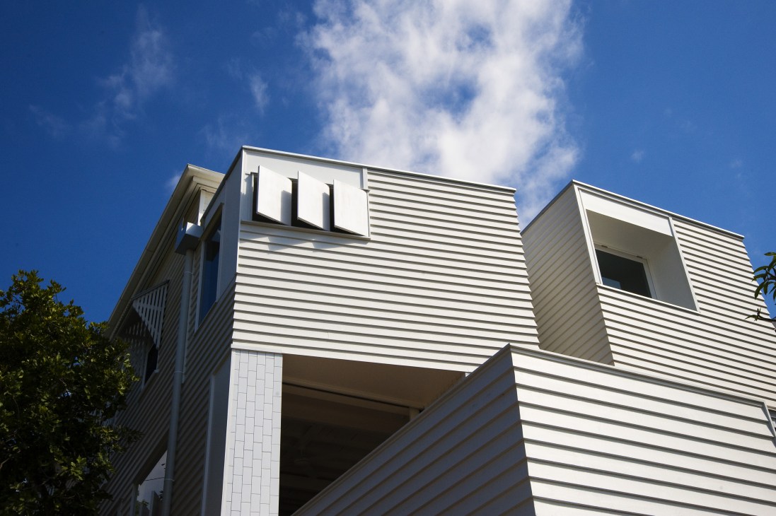 Contemporary white weatherboard towers with ventilation shutters and large windows against a blue sky.
