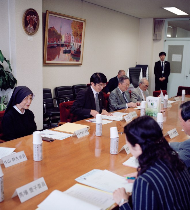 Mayor Tomihisa Taue seated at a conference table with local business leaders and university heads during a formal meeting.