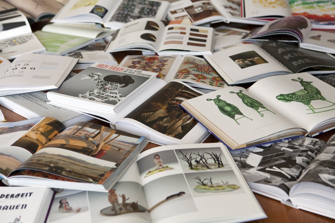 A collection of open art books displayed showing diverse imagery including botanical illustrations, photography, and graphic designs.
