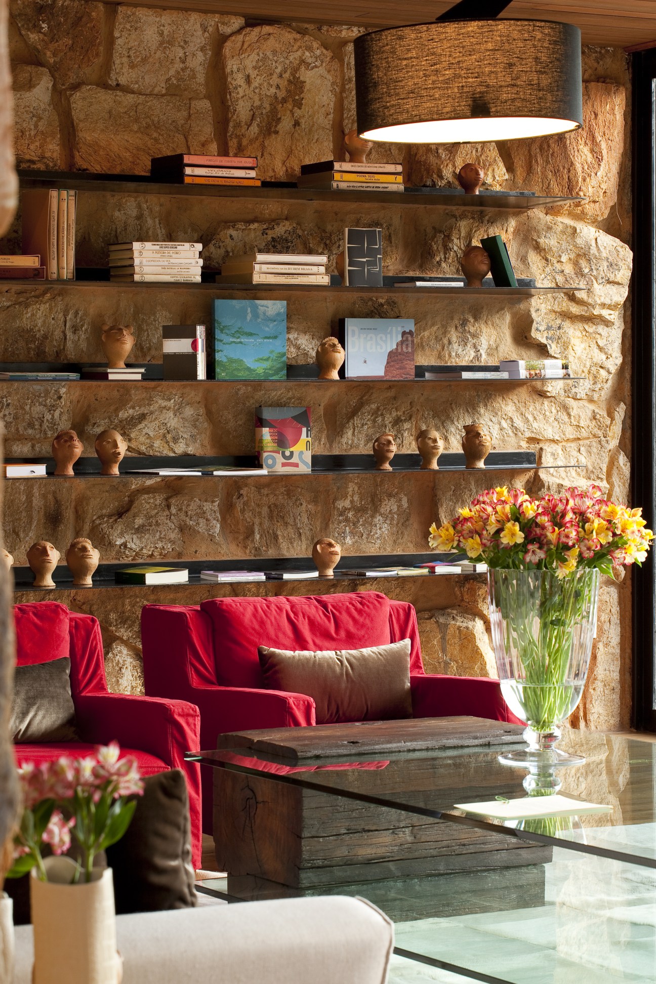 Interior library shelving with stone walls, books, decorative objects, and red velvet seating below at Botanique Hotel and Spa.