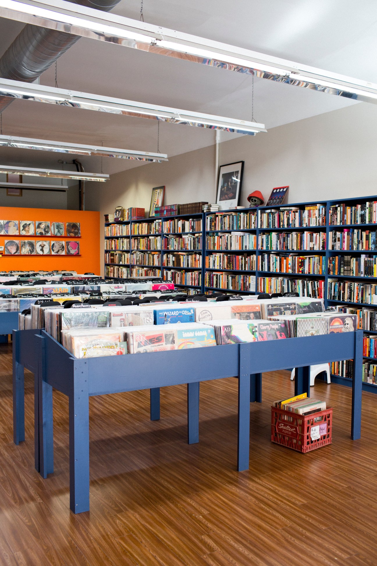 Interior of Pandemonium Books & Discs showing blue display table with vinyl records, floor-to-ceiling shelves of books, and orange accent wall.