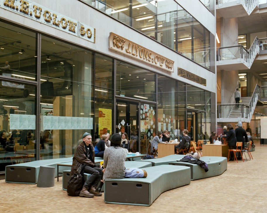 Students and visitors gather in a modern atrium space with glass storefronts and vintage signage collected by the graphics department.