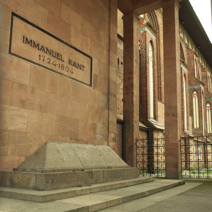 Stone tomb with plaque reading 'Immanuel Kant 1724-1804' at the base of Kaliningrad Cathedral's brick wall.