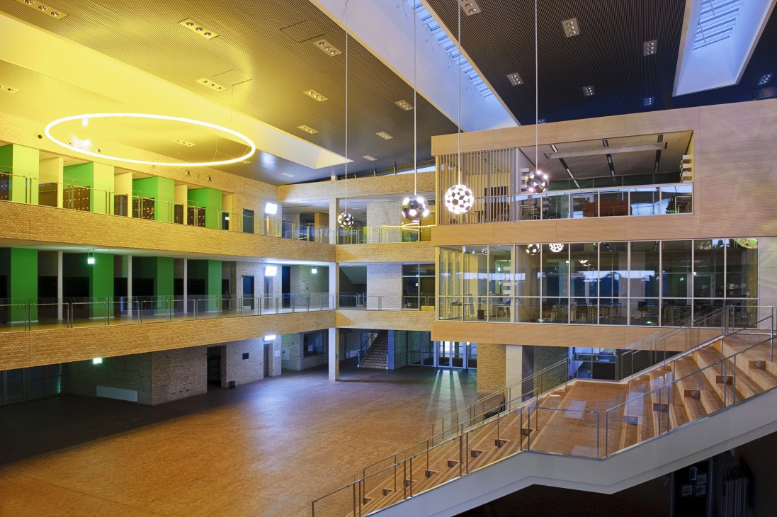Bright multi-level atrium with balconies, glass walls, hanging spherical light art installation, and green lockers.