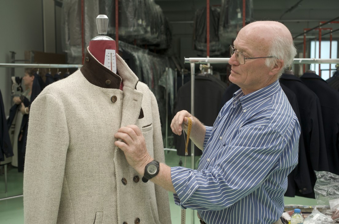 Tailor Albino Lavo measuring a cream-colored wool jacket on a dress form in his workshop.