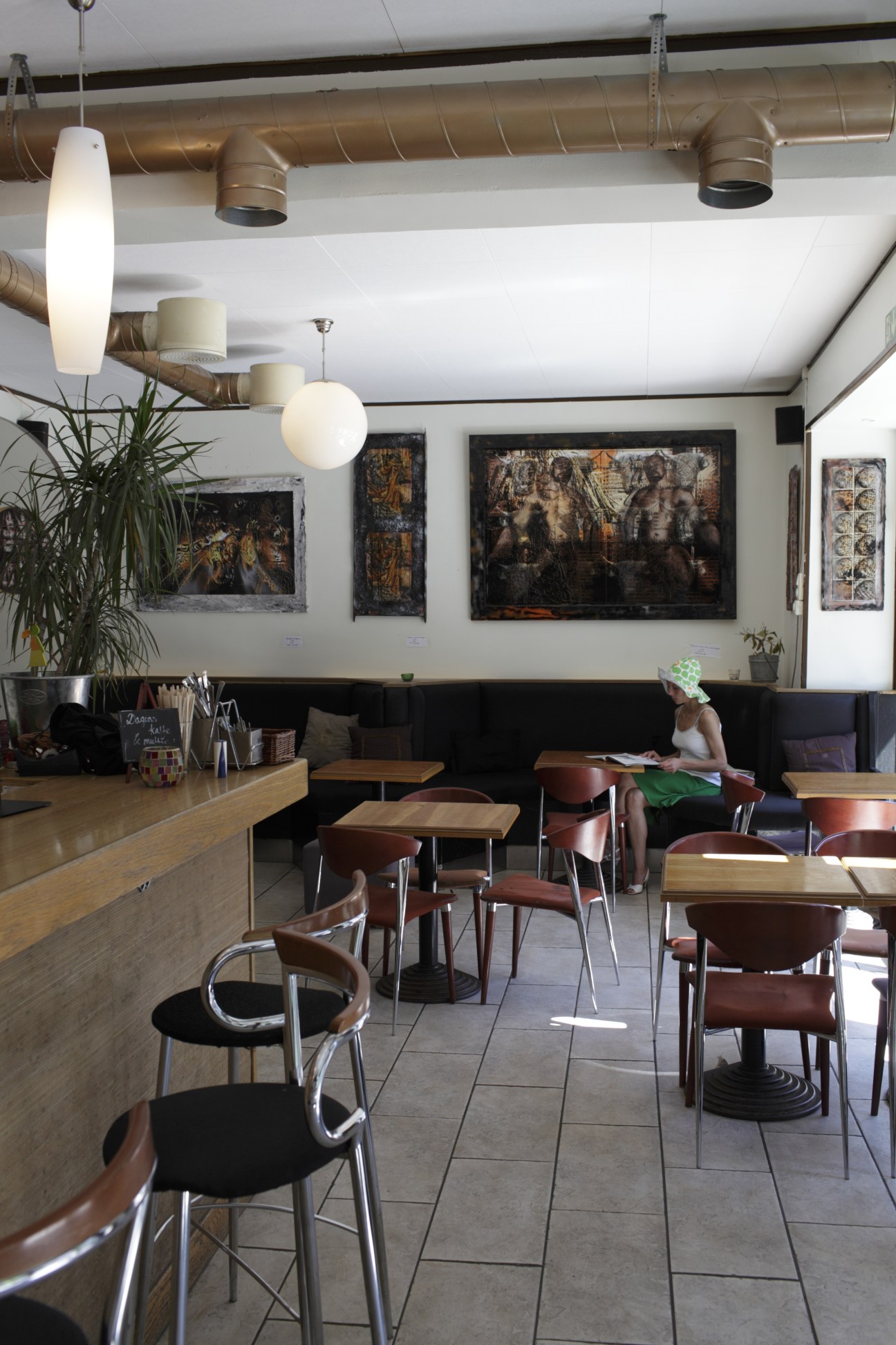 Modern café interior with pendant lights, wooden tables, brown leather chairs and dark artwork on white walls.